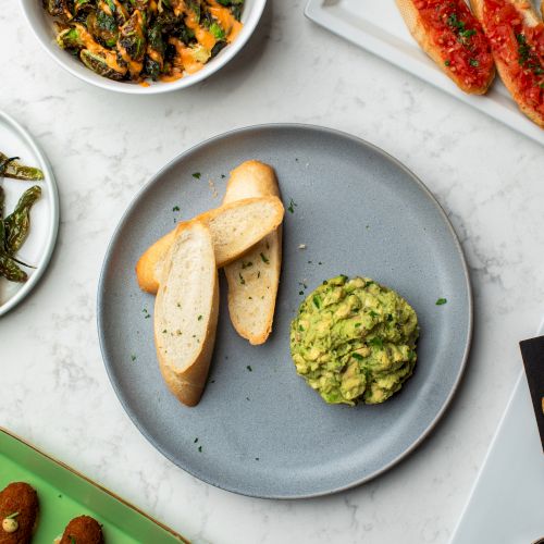 The image shows a spread of dishes: vegetable salad, baguette slices with tomato topping, a green mixture, and croquettes on platters.