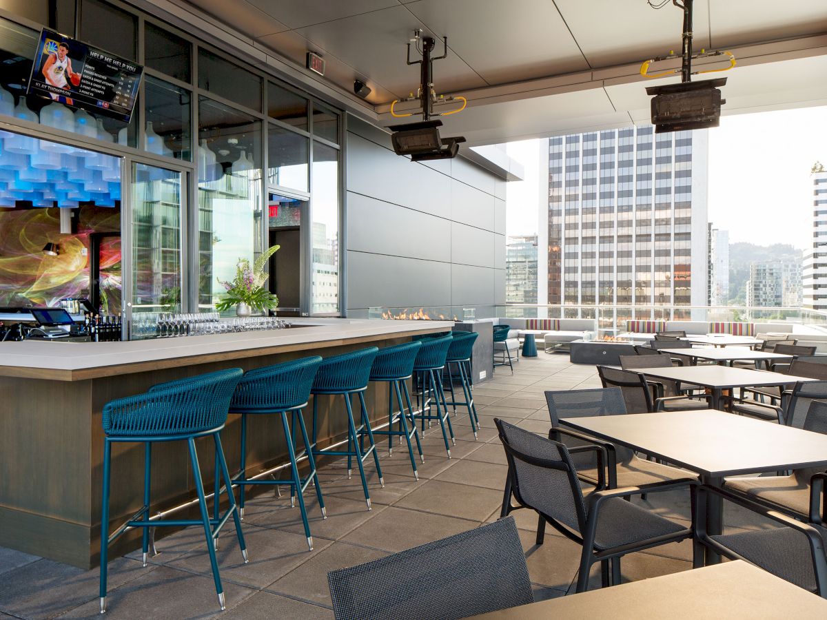 An outdoor rooftop bar and dining area with tables, chairs, and city views.